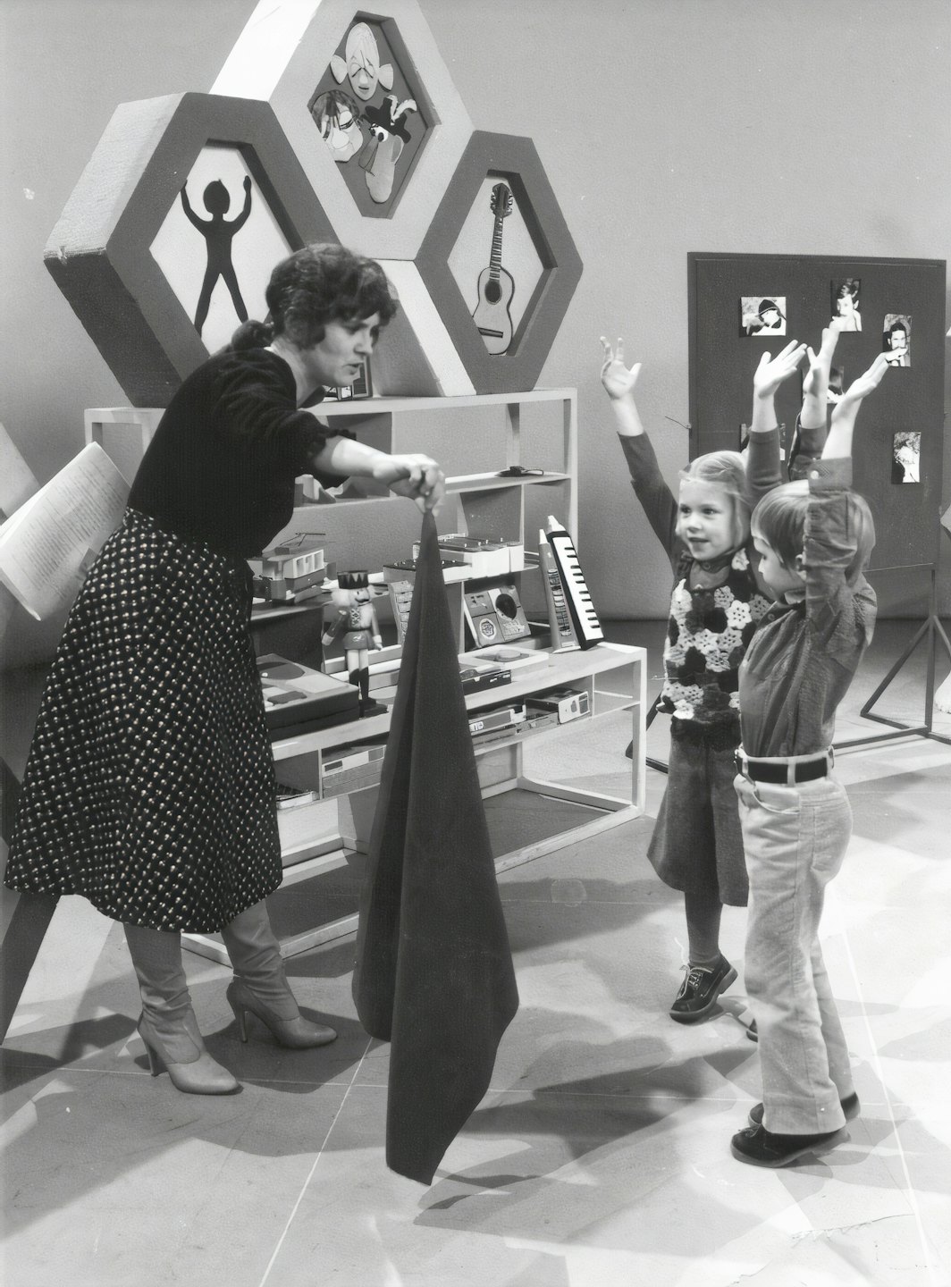 Eine Präsentatorin zeigt zwei begeisterten Kindern in einem Studio Stoff.