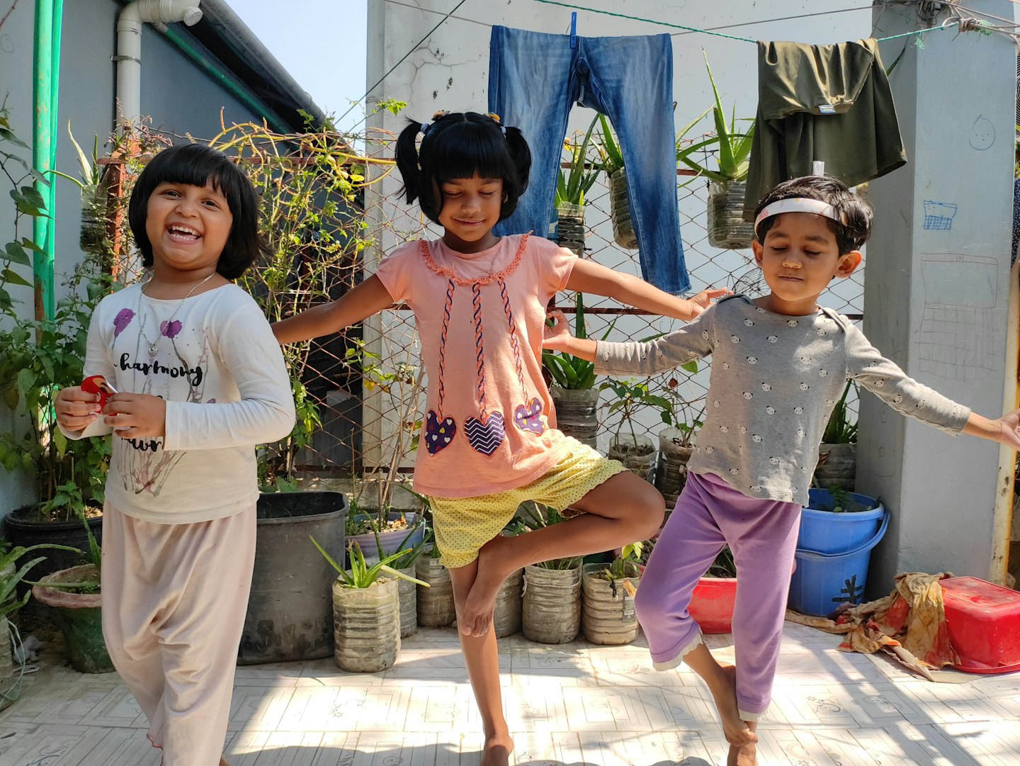 Drei Kinder spielen an einem sonnigen Tag draußen mit Wäsche im Hintergrund.